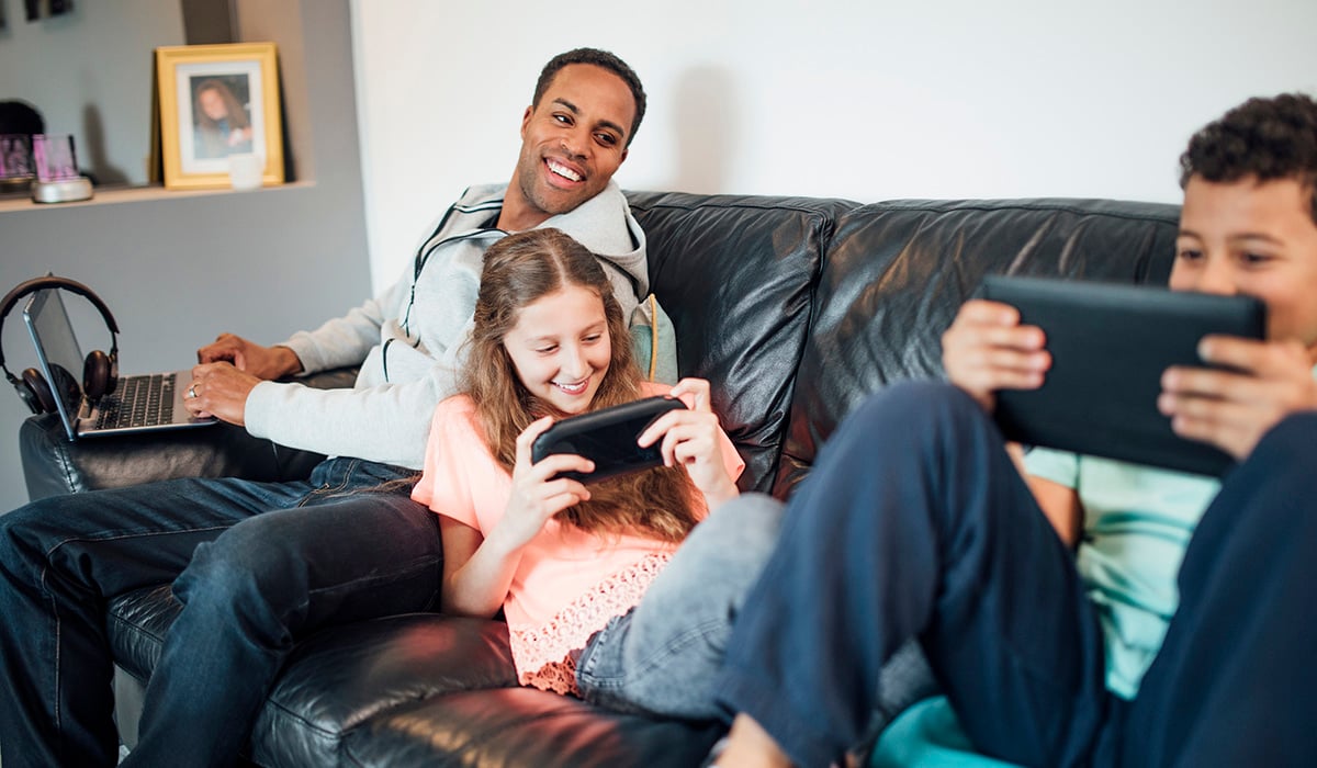 Family sitting on the sofa playing games on devices