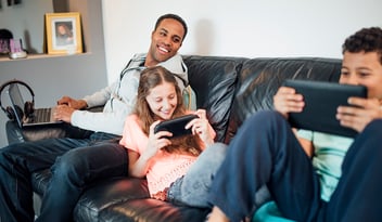 Family sitting on sofa playing games on various devices