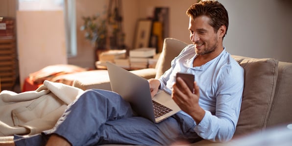 A man using his phone and laptop to browse at home.