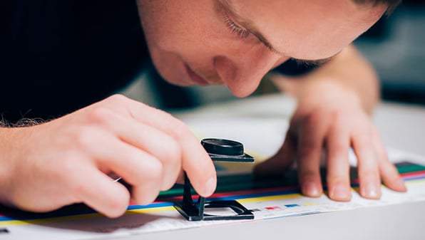 Man using a magnifying glass to inspect a print job.